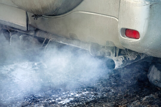 Car engine smoking, smoking exhaust pipe, closeup. Blue exhaust smoke. Car with gasoline or diesel  engine. Engine warming up at idle in winter season.