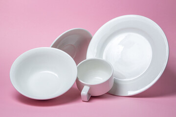 A set of white dishes on a pink background. A set of plates, saucers and cups.