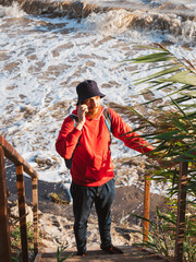 Bearded millennial man in red hoody backpack with smartphone taking photo of autumn sea dry reeds. Authentic male tourist Blogger guy lifestyle Solo travel adventure concept Active walking backpacking