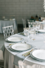 glass glasses and white plates. table setting in the interior of the restaurant. The decor of the festive table. In gray-silver tones with gold cutlery. Luxury wedding, party, birthday.
