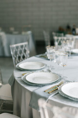 glass glasses and white plates. table setting in the interior of the restaurant. The decor of the festive table. In gray-silver tones with gold cutlery. Luxury wedding, party, birthday.