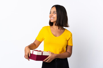 Young latin woman holding a gift isolated on white background looking side