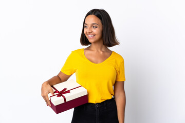 Young latin woman holding a gift isolated on white background looking to the side and smiling