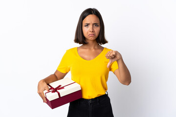 Young latin woman holding a gift isolated on white background showing thumb down with negative...
