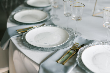 glass glasses and white plates. table setting in the interior of the restaurant. The decor of the festive table. In gray-silver tones with gold cutlery. Luxury wedding, party, birthday.