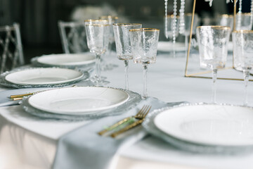 glass glasses and white plates. table setting in the interior of the restaurant. The decor of the festive table. In gray-silver tones with gold cutlery. Luxury wedding, party, birthday.