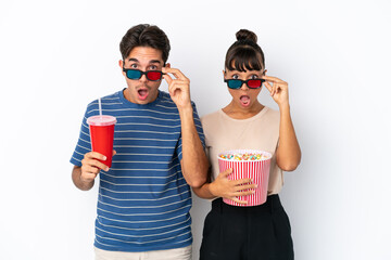 Young mixed race friends isolated on white background surprised with 3d glasses and holding a big bucket of popcorns