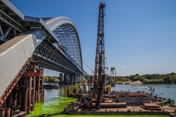 Obraz premium Construction of a large arched bridge in the capital of Ukraine. Podolsky bridge, panoramic view of the bridge under construction across the Dnipro, clear weather, summer. Kyiv