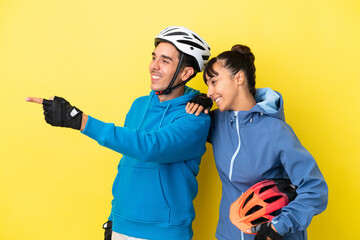 Young cyclist couple isolated on yellow background pointing to the side to present a product