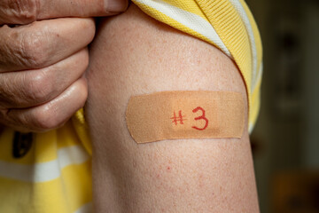 Senior caucasian man holding up shirt sleeve to show the bandaid after the booster coronavirus...