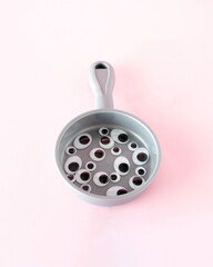 A gray frying pan full of black eyes. Minimal Halloween concept
