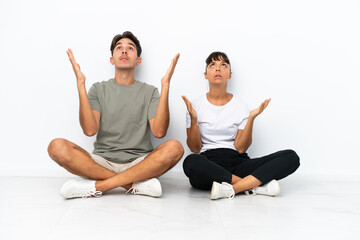 Fototapeta na wymiar Young mixed race couple sitting on the floor isolated on white background frustrated by a bad situation