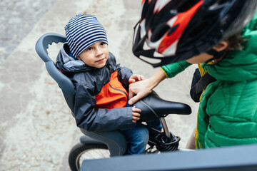 European father in protective helmet and green jacket taking his son after school or kindergarten at home with bicycle. Happy family concept.