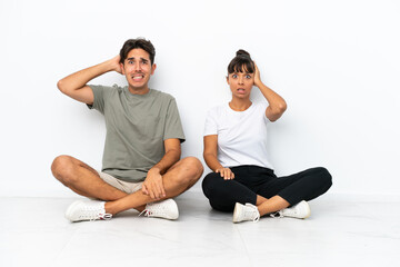 Fototapeta na wymiar Young mixed race couple sitting on the floor isolated on white background takes hands on head because has migraine