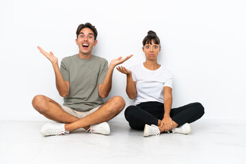 Young mixed race couple sitting on the floor isolated on white background holding copyspace imaginary on the palm to insert an ad