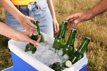 Friends taking bottles of beer from cool box outdoors, closeup