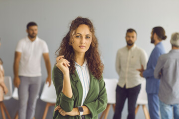 Portrait of successful confident businesswoman. Good looking young business woman with wavy brown hair, in elegant jacket and mockup blank face hand watch standing in office and looking at camera