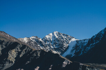 Atmospheric mountain landscape with dark mountains silhouettes. Sharp rocky pinnacle and snow-covered top in sunlight. Alpine scenery with black orange mountain with peaked top in sunshine in autumn.