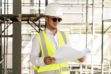 Fototapeta na wymiar Man architect wearing safety vest with a blueprints on a construction site