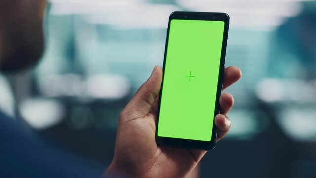 Black Man with Green Screen Chroma Key Smartphone in Office. African-American Person using Internet, Social Media, Online Shopping with Mobile Phone Device. Focus on Display, Hand