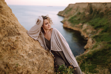 Curly woman posing at the edge of a rock above the sea, with blue sky and sea background. Autumn style. Travel and adventure.