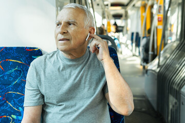 Elderly man is using wireless earbuds during ride in public transport