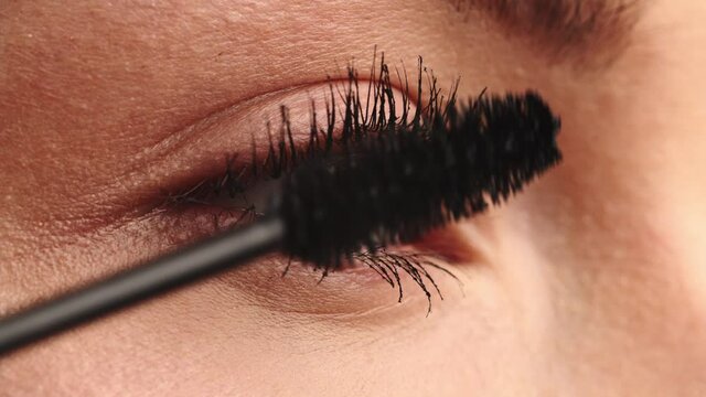 Closeup shot, stylist applies black mascara  on the eyelashes of the female eye. Woman making make up using black mascara. Professional makeup.  Making mua. Slow motion. Tutorial makeup master class