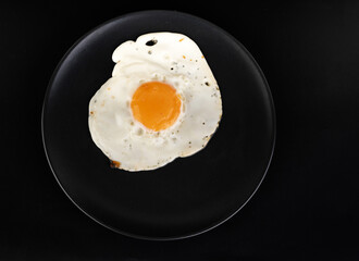 Scrambled eggs with chicken eggs on a black plate on a black background