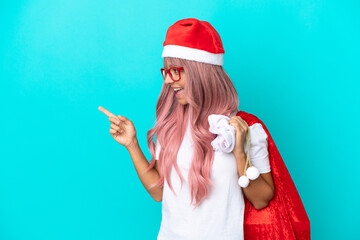 Fototapeta na wymiar Young mixed race woman handing out gifts on Christmas isolated on blue background pointing finger to the side and presenting a product