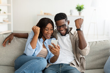 African american couple using cellphone, celebrating win - Powered by Adobe