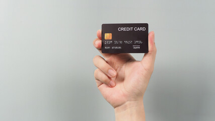 Hand is holding black credit card isolated on grey background.