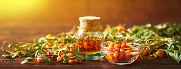 Glass bottle with sea buckthorn oil berries and sea buckthorn branches on wooden background - obrazy, fototapety, plakaty