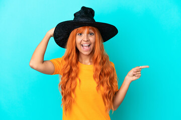 Young woman disguised as witch isolated on blue background surprised and pointing finger to the side