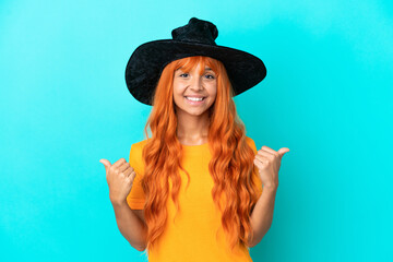 Young woman disguised as witch isolated on blue background with thumbs up gesture and smiling