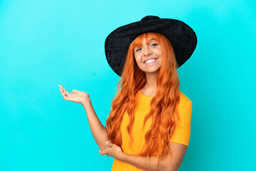 Young woman disguised as witch isolated on blue background extending hands to the side for inviting to come