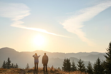 Couple enjoying sunrise in mountains, back view. Space for text