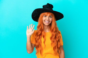 Young woman disguised as witch isolated on blue background saluting with hand with happy expression
