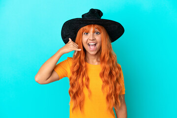 Young woman disguised as witch isolated on blue background making phone gesture. Call me back sign