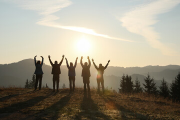 Group of people enjoying sunrise in mountains, back view