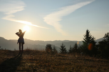 Woman enjoying sunrise in mountains, back view. Space for text