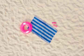Striped beach towel, flip flops and swim ring on sand, aerial view