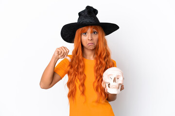Young mixed race woman disguised as witch holding a skull isolated on white background showing...