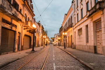 Old center of the city of Santos. Street of trade. Stone street, facades of old houses, old cast iron poles with yellow light and in the background the church of Valongo.