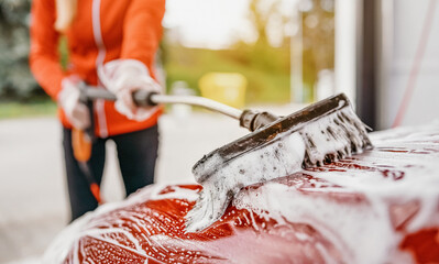 Young woman cleaning her car in self serve carwash. Closeup detail on white soap foam and brush...