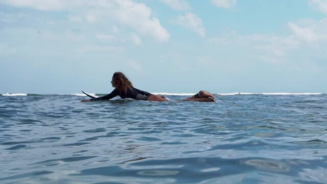 Video footage of surfer girl on white surf board in blue ocean pictured from the water in Bali