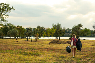 Woman with trash bags full of garbage outdoors, back view. Space for text