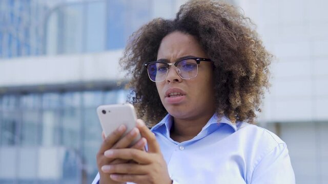 Scared young afro-american woman reading message on smartphone, confused face expression. Nervous black female facing cyber bullying in social media. Distressed company employee having panic attack