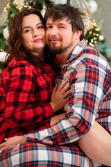 Fototapeta premium in love and happy man and woman in red checkered pajamas at the Christmas tree.
