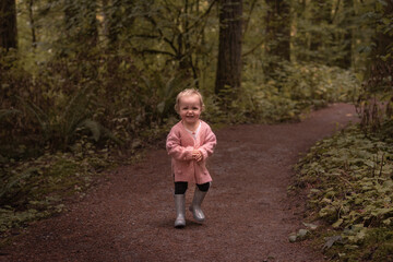 Fototapeta premium Curly haired cute toddler girl in pink sweater outdoors on forest hiking trail path