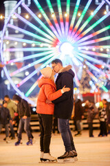 A young Caucasian couple spends the New Year and Christmas holidays in an active and sporty manner on the city ice arena on the square in the city. Romantic evening on valentine's day at the rink